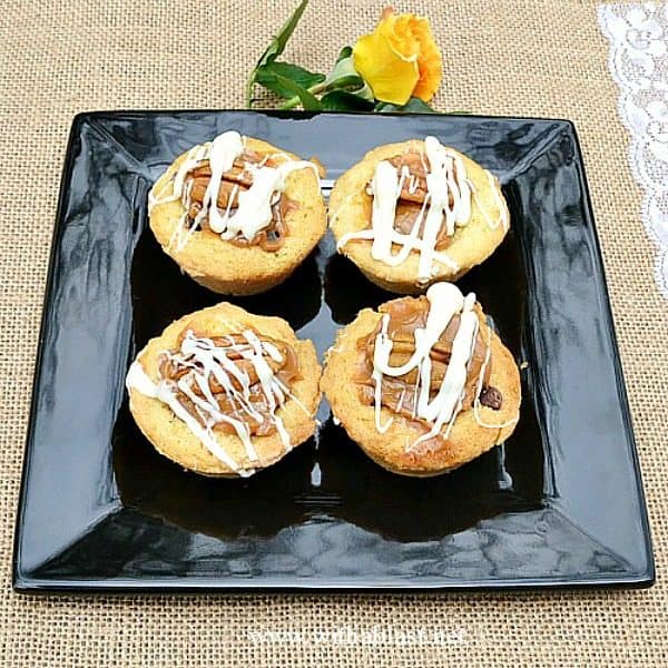 Quick, easy and delicious Cookie Cups filled with Chocolate Chips, chopped Pecans, Caramel and topped with another Pecan Nut and drizzled with White Chocolate 
